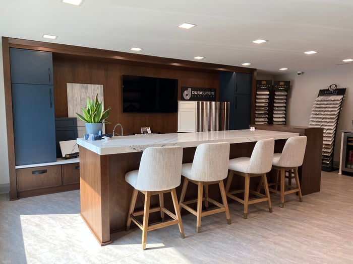 Modern design studio featuring a long bar-height counter with four comfortable bar stools, showcasing an array of home remodeling design samples, including tile, wood, and fabric swatches.